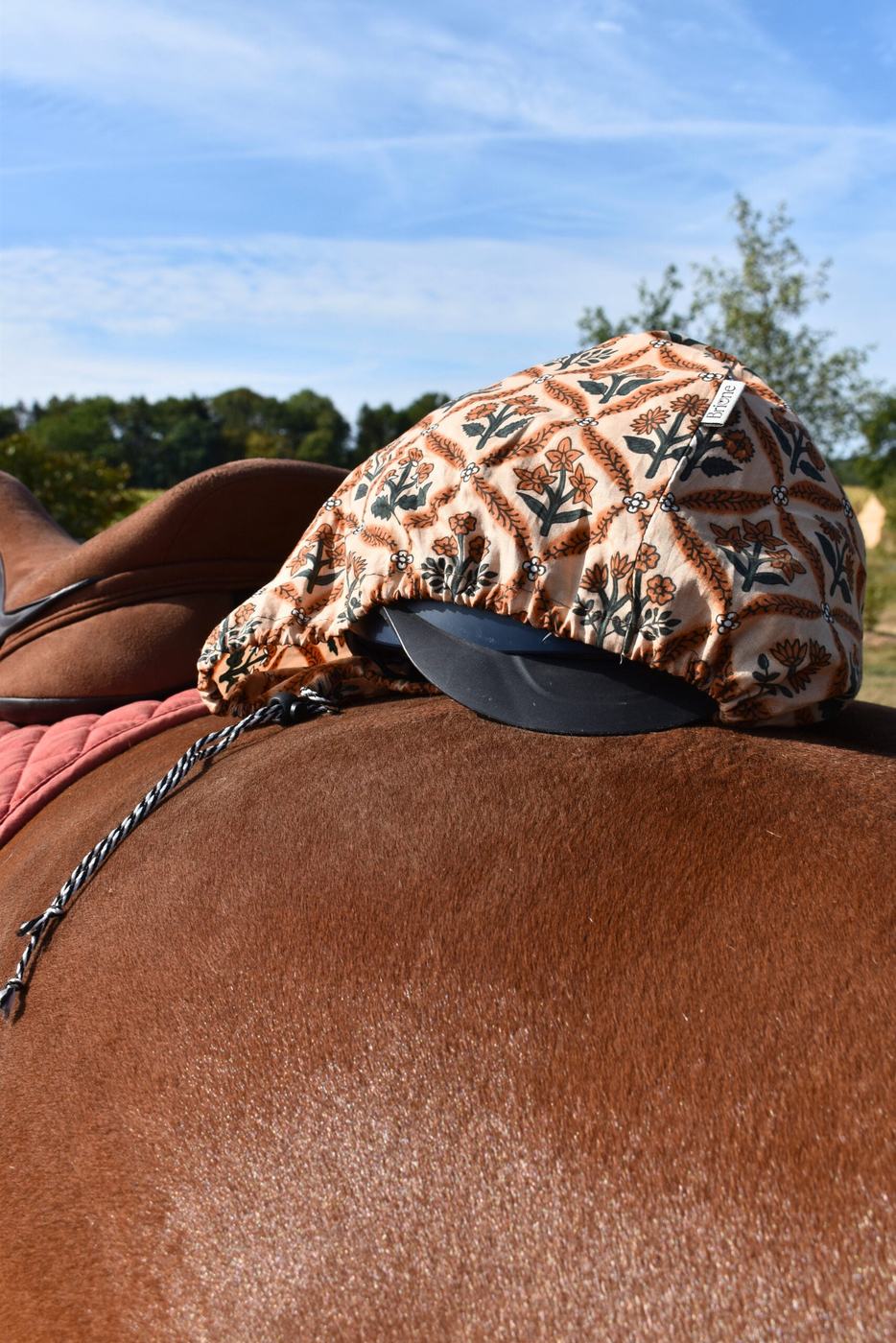 housse de bombe en coton léger marron; légèrement ouverte, posée sur la croupe d'un cheval bai